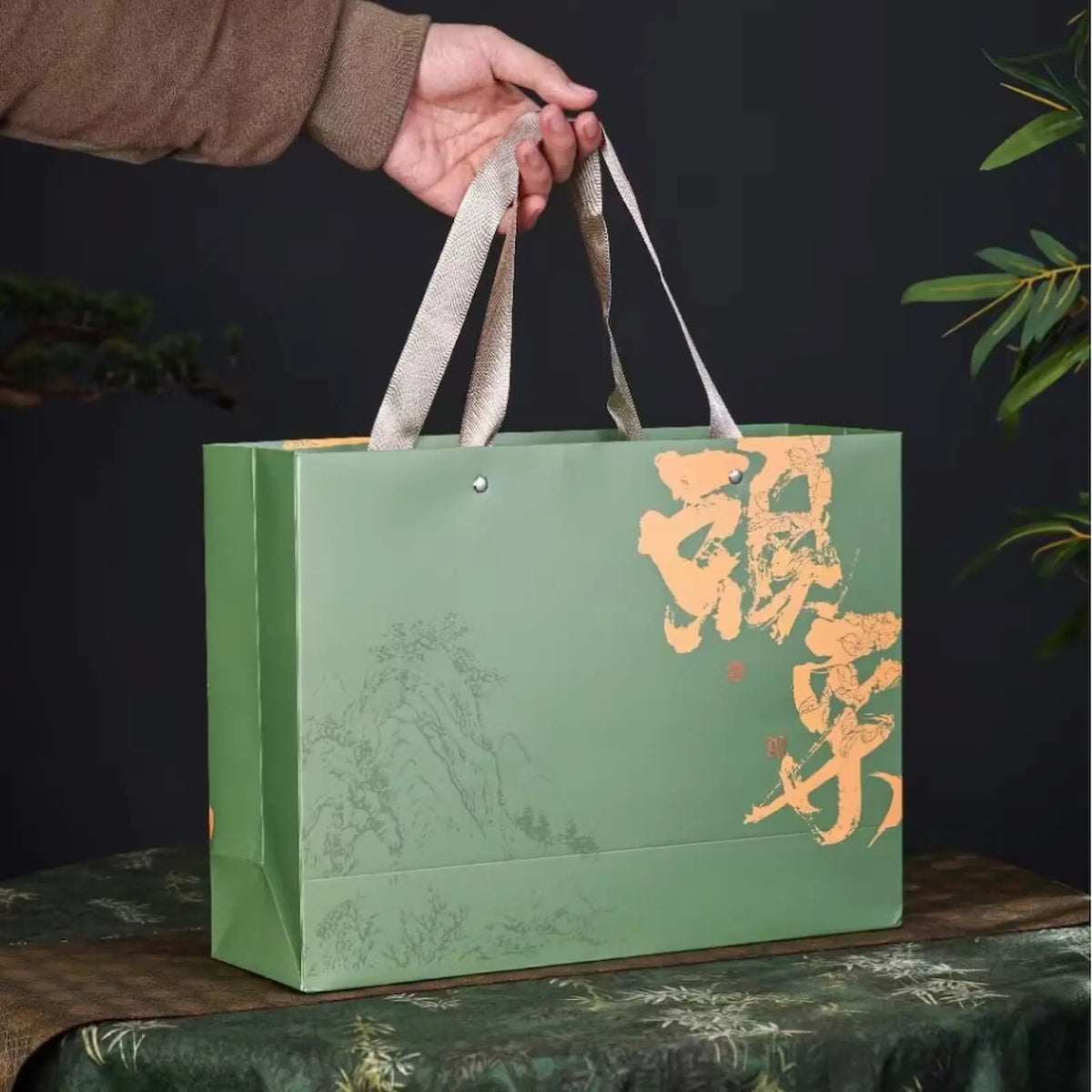 Green Ming Qian Longjing tea gift bag with traditional Chinese calligraphy and subtle landscape art, sturdy handles for easy carrying. Perfect for presenting premium pre-Qingming West Lake Dragon Well green tea on holidays and special occasions.
